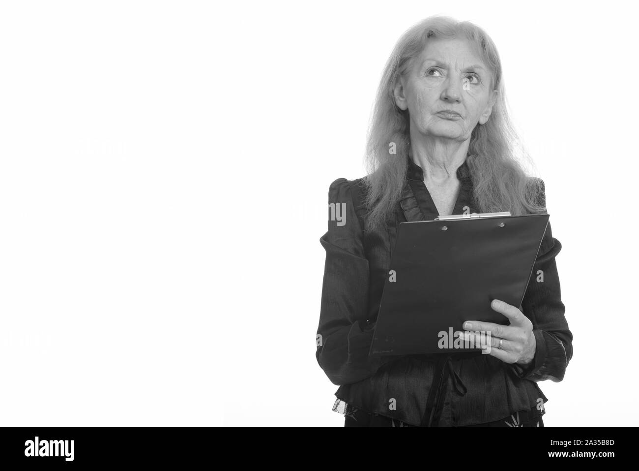 Studio shot of senior businesswoman holding clipboard en pensant Banque D'Images
