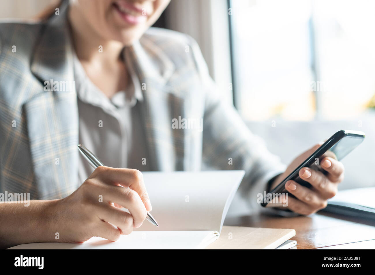 Jeune femme contemporaine avec stylo et téléphone l'écriture de plan de travail Banque D'Images