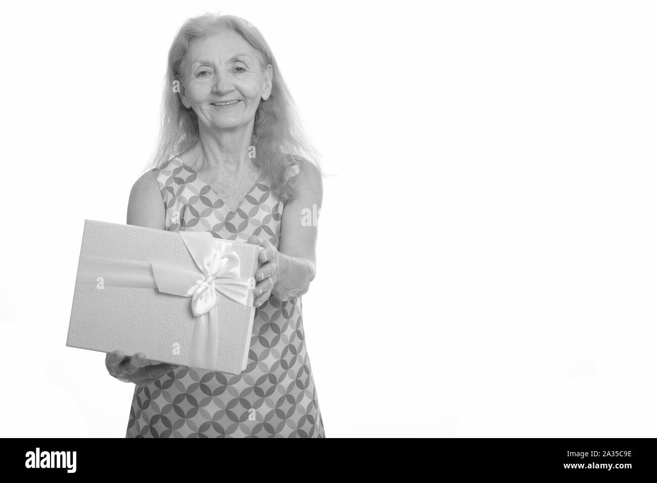 Studio shot of senior woman smiling and giving gift box Banque D'Images
