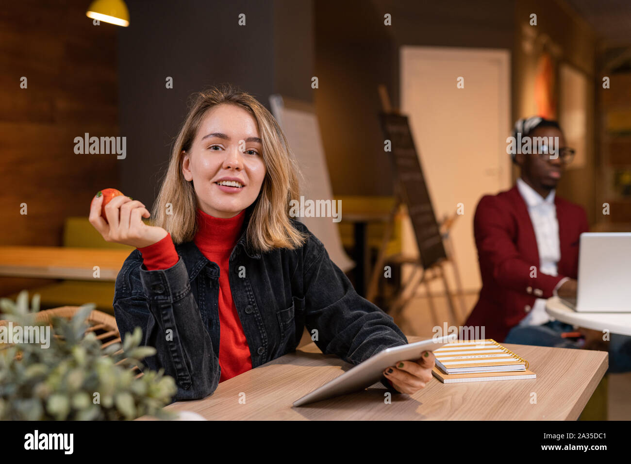 Jeune blonde avec des étudiants occasionnels et tablette Apple rouge assis par table Banque D'Images