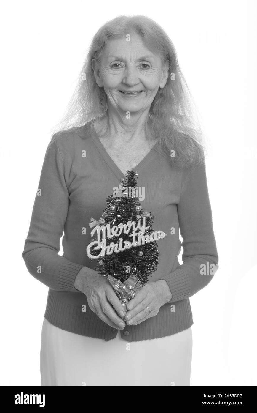 Studio shot of senior woman smiling while holding Merry Christmas Tree Banque D'Images