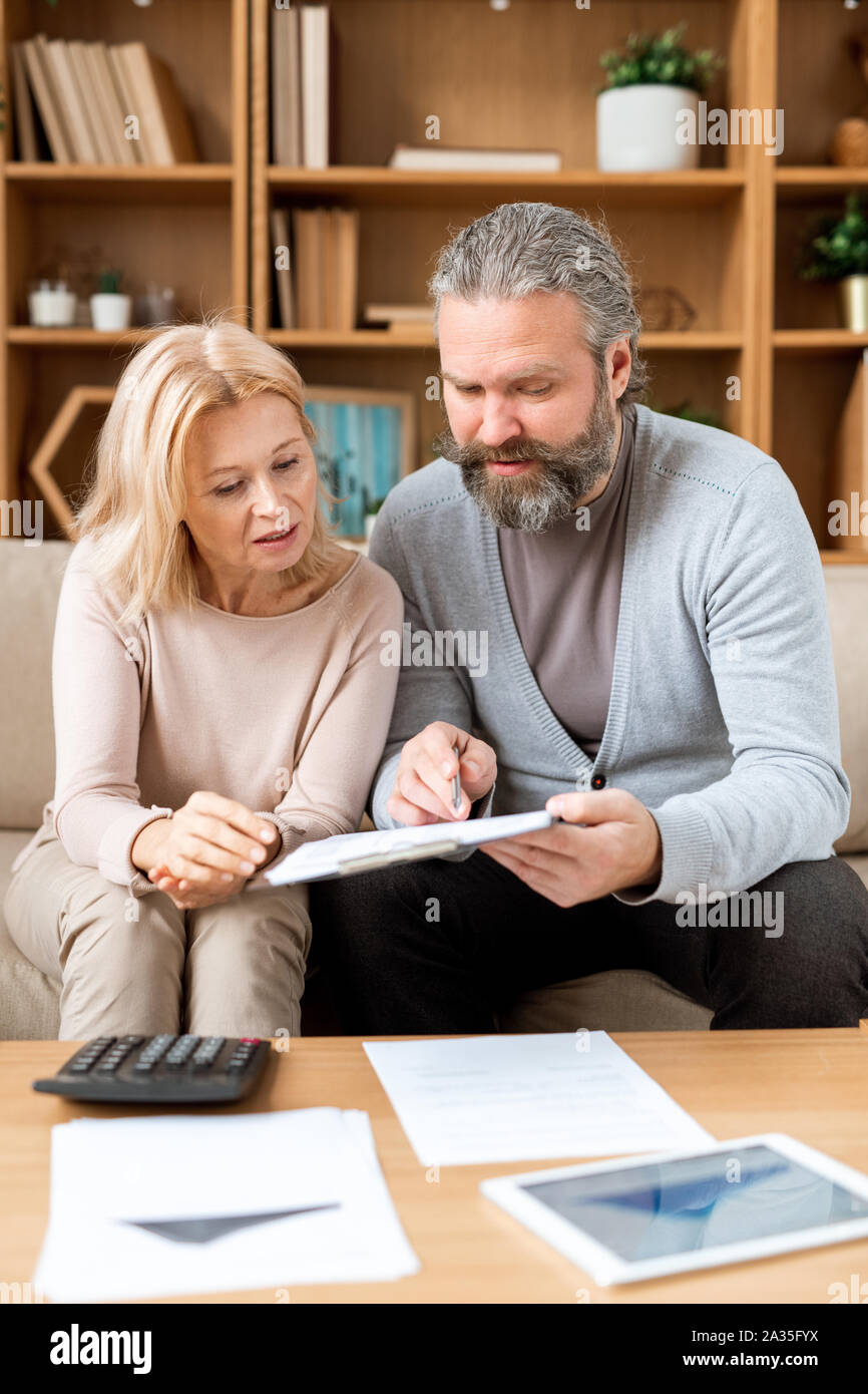 Femme mature à l'écoute de son mari pointant sur le document en la lisant Banque D'Images