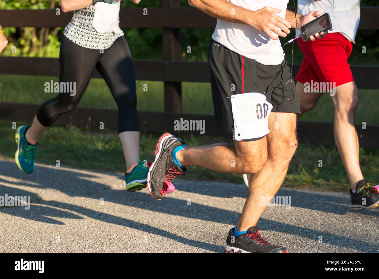 Les personnes exécutant une course en début de soirée à Belmont Lake State Park. L'un d'eux est à l'écoute de la musique avec son téléphone Banque D'Images