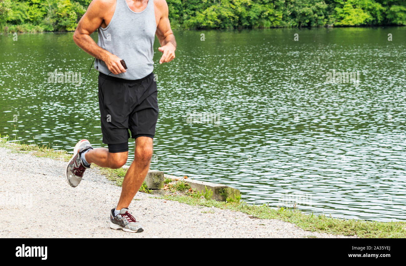 Un coureur est maintenant sur leur téléphone lors de l'exécution d'une course dans les bois, passant d'un lac. Banque D'Images