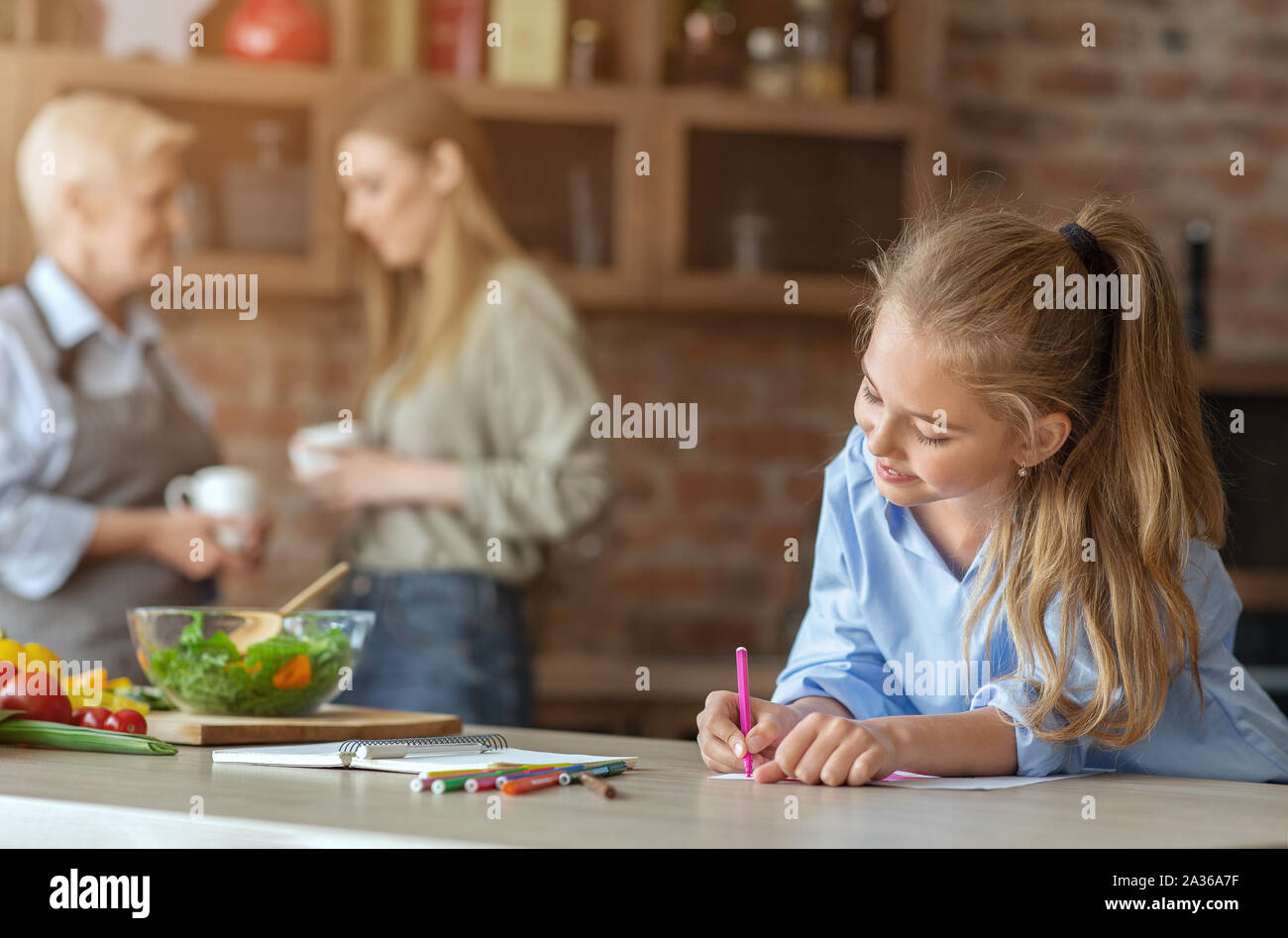 Petite fille en peinture à cuisine tout en aidant la maman et mamie Banque D'Images