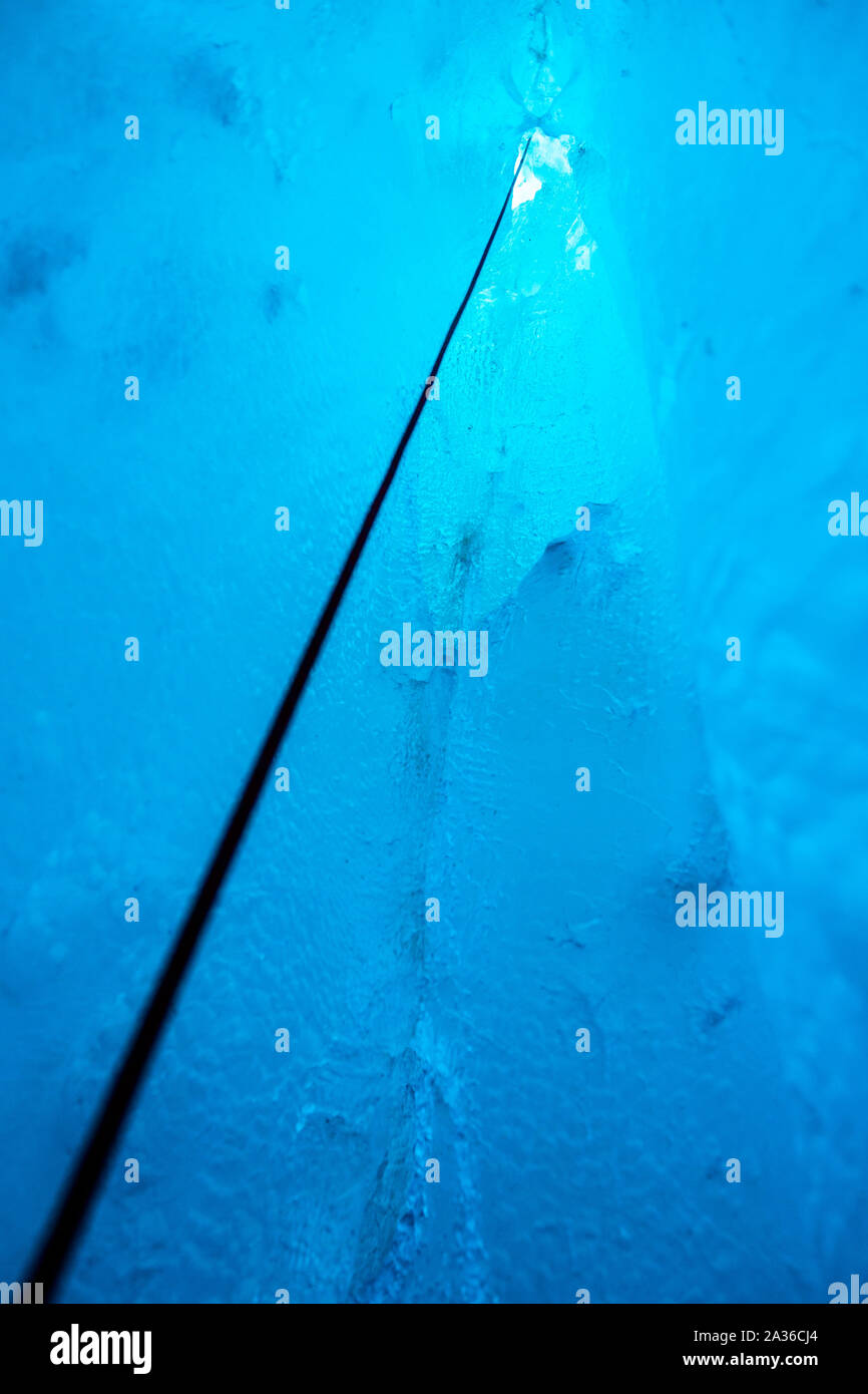 Jusqu'à la corde pour une entrée étroite dans une grotte de glace sur le glacier du saumon au Canada. Entouré par de beaux bleu clair à l'intérieur de la caverne de glace. Banque D'Images