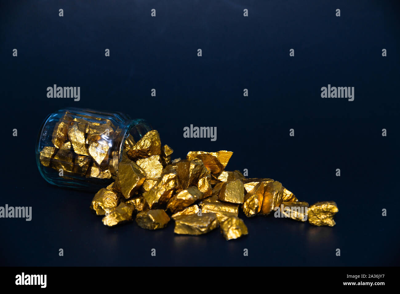 Des pépites d'or, le minerai d'or , pierre précieuse ou forfaitaire en pierres dorées et bocal en verre dans une pièce sombre. Banque D'Images