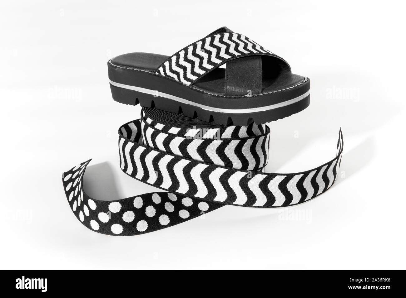 Noir et blanc sandale d'été avec l'empeigne élastique affiché sur un rouleau de ruban élastique de la comparaison sur un fond blanc dans une industrie de la mode et Banque D'Images
