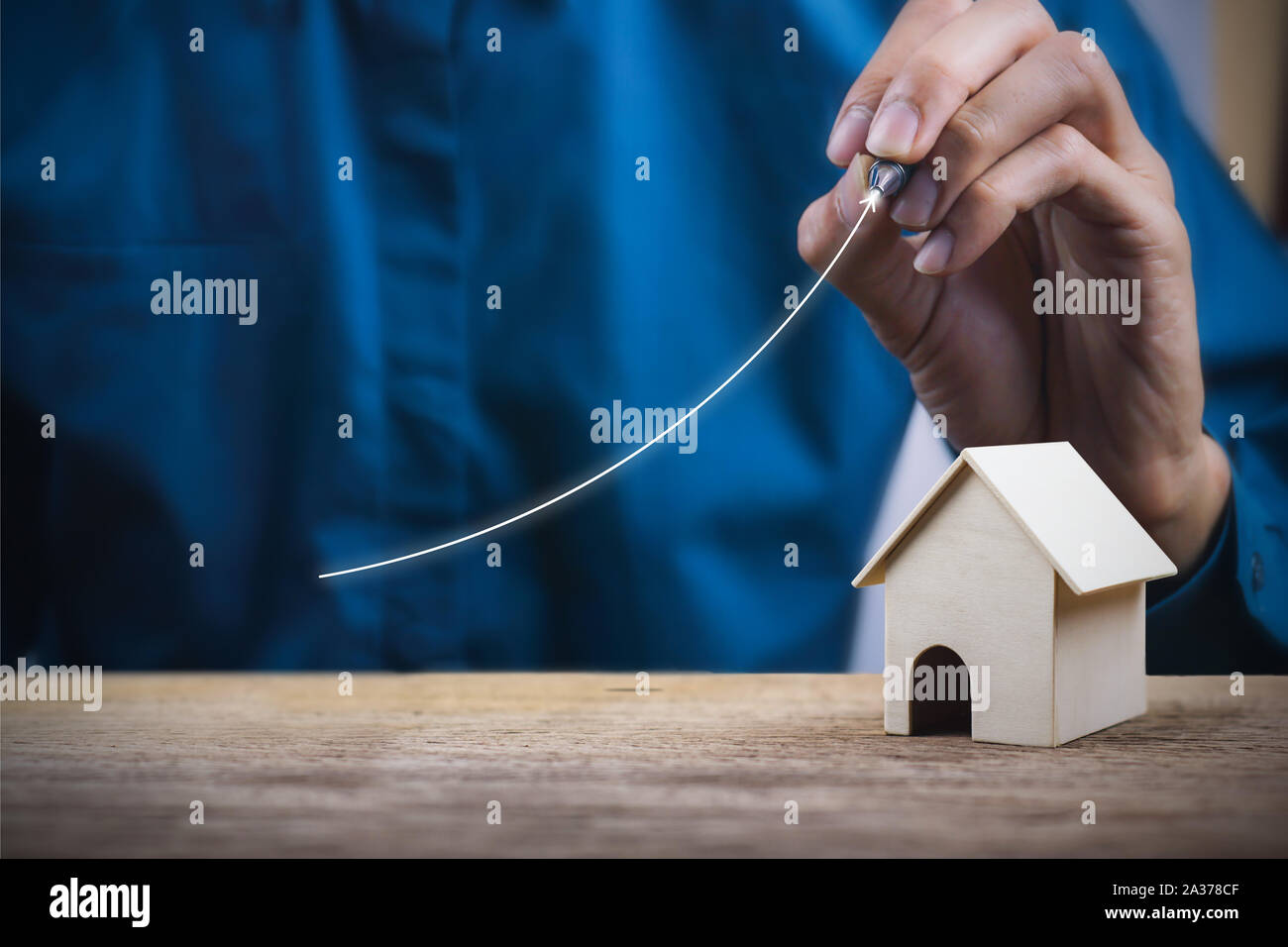 Concept de croissance de la propriété. Un homme d'affaires en hausse d'écriture graphique avec une petite maison modèle sur table en bois. Banque D'Images