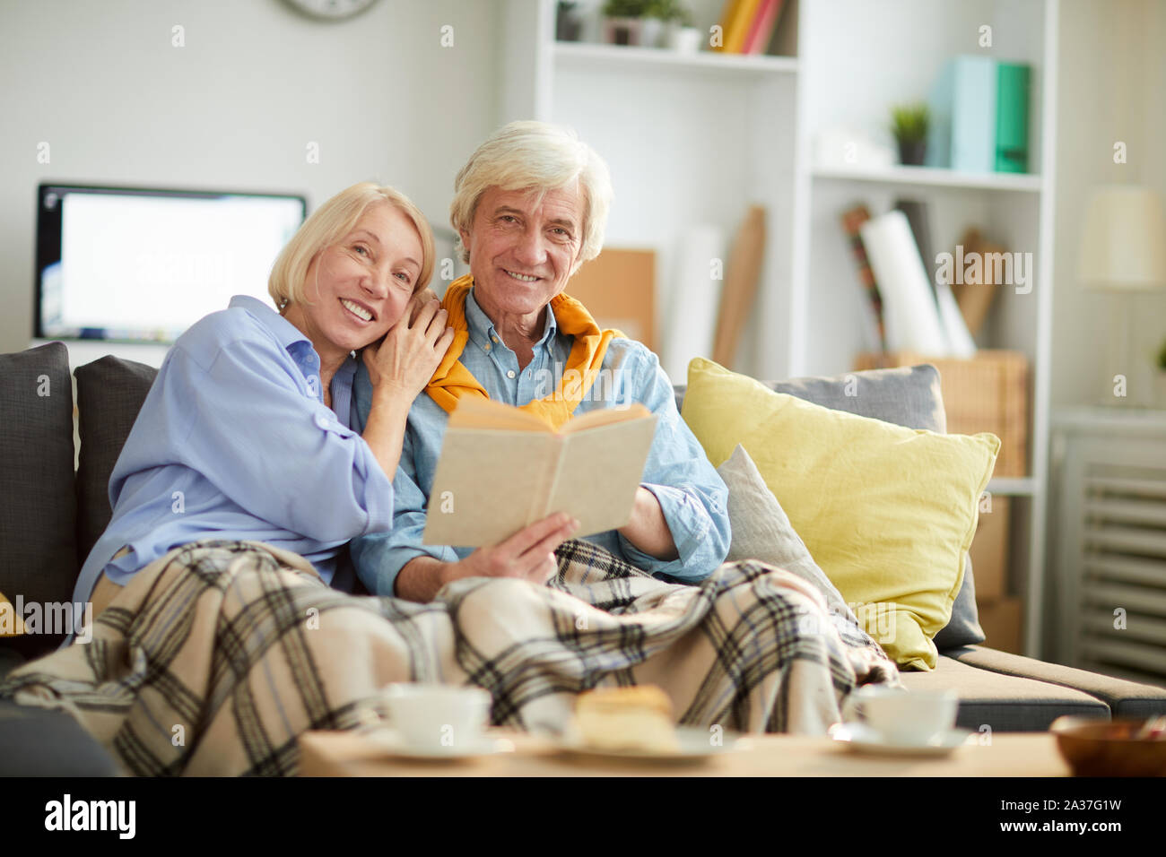 Portrait of senior woman looking at camera while reading book together sitting on sofa at home, copy space Banque D'Images