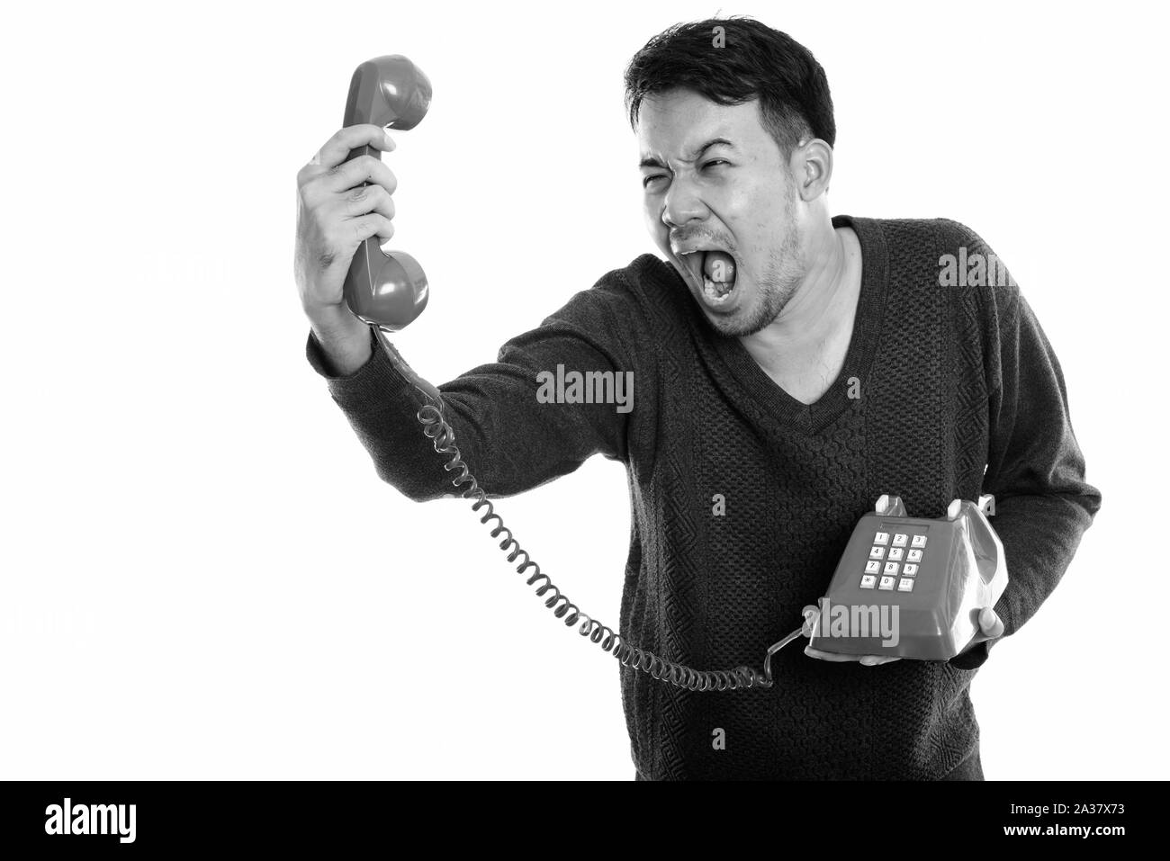 Studio shot of young man holding asiatique en colère et de crier à l'ancien téléphone Banque D'Images