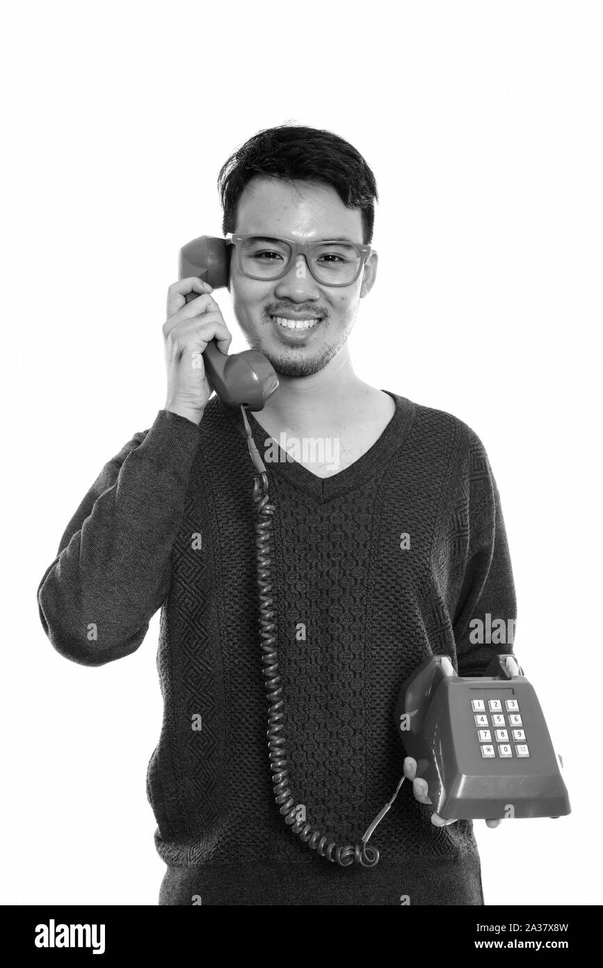 Studio shot of young happy Asian man smiling, tout en parlant de vieux téléphone Banque D'Images