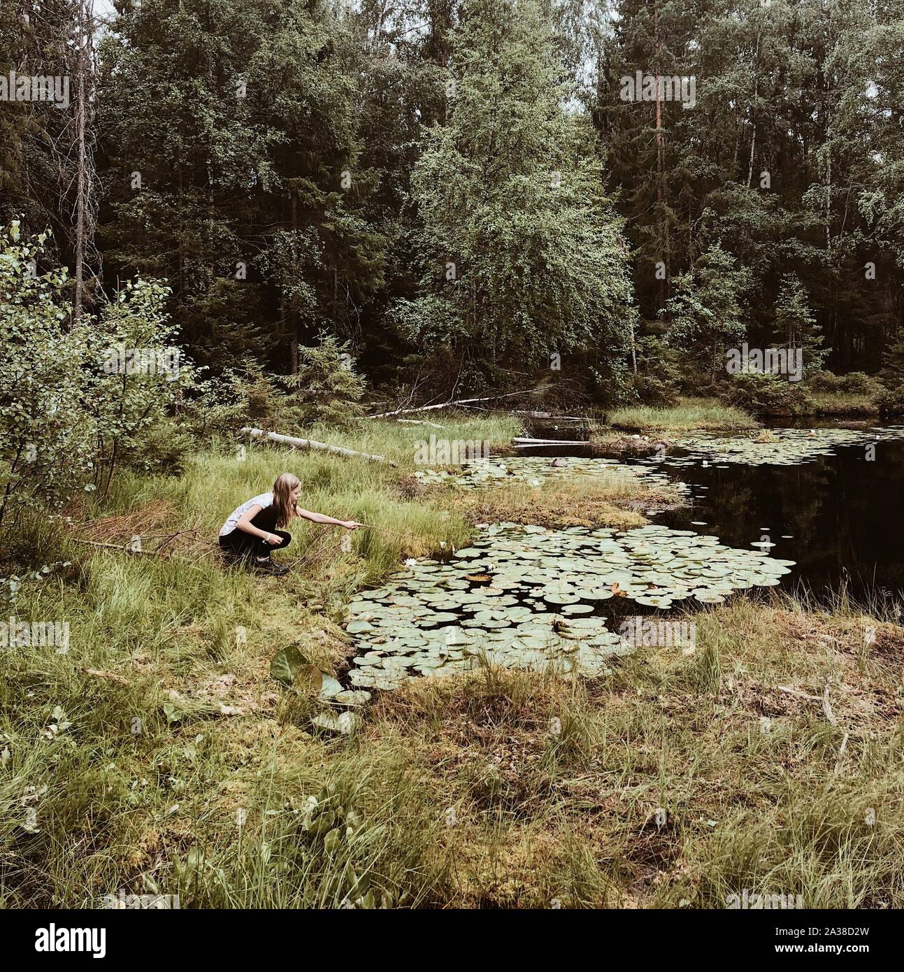 Girl crouching par une rivière tenant un bâton, Norvège Banque D'Images