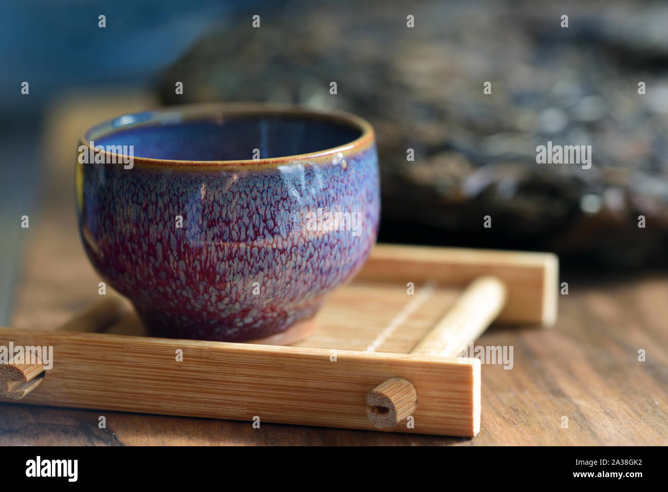 Libre d'une tasse en céramique mouchetée bleu, sur une planche en bois, avec un gâteau de thé dans l'arrière-plan pour une cérémonie du thé Banque D'Images