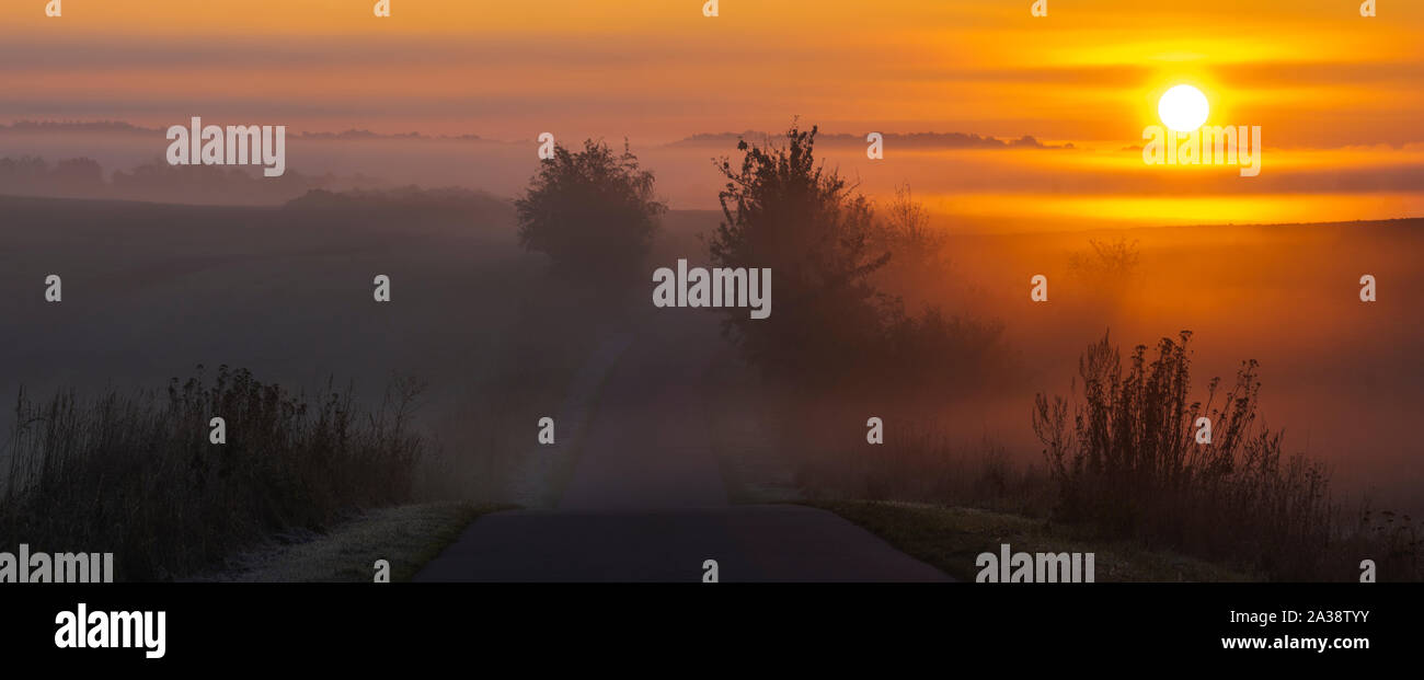 Lever du soleil par la route et dans les champs qui rappelle le paysage de la Toscane Italienne sur un beau matin brumeux Banque D'Images