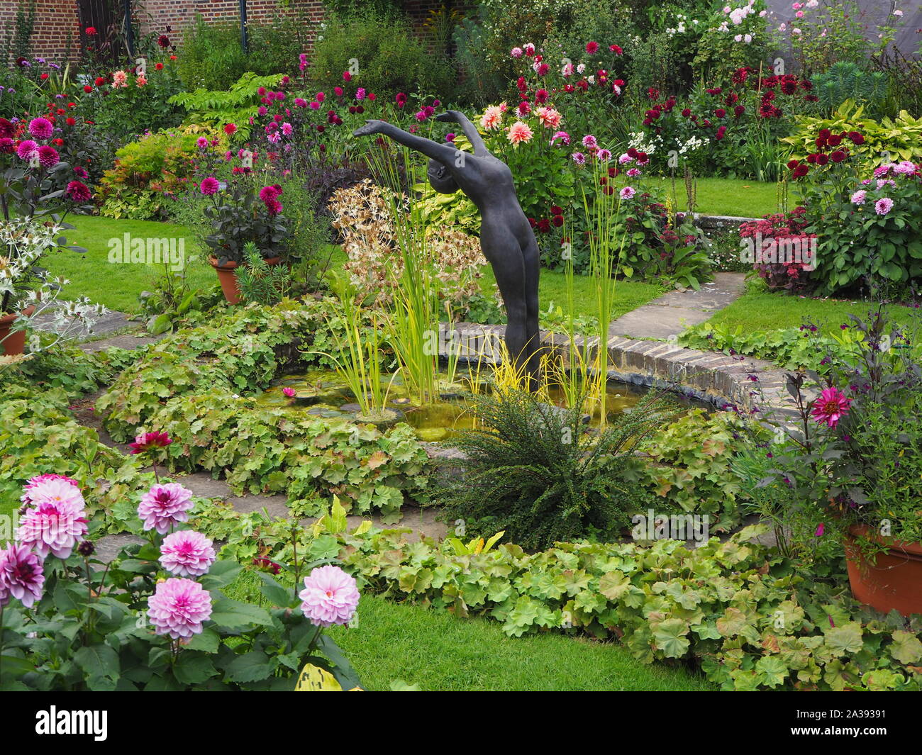 Chenies Manor jardin en contrebas de l'étang ornemental avec Alan Biggs sculpture dans le centre avec Dahlia 'Crème de Cassis', 'Labyrinthe' et divers feuillages. Banque D'Images