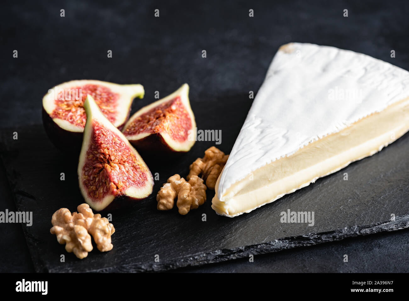 Brie ou camembert plaque avec les figues et les noix servi sur ardoise noire Banque D'Images