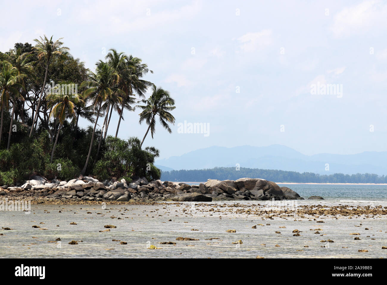 Tropical beach, vue sur la mer et l'île verte avec des cocotiers. Paysage paradisiaque avec côte rocheuse et de montagnes au loin Banque D'Images