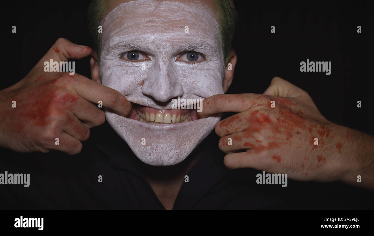 Clown Halloween Man Portrait. Close-Up D'un Fou, Evil Clowns Font Face.  Maquillage Visage Blanc. Des Cheveux Verts. Sourire Effrayant Avec Les  Doigts. Modèle Attrayant En Costume D'halloween. Fond Sombre Photo Stock -