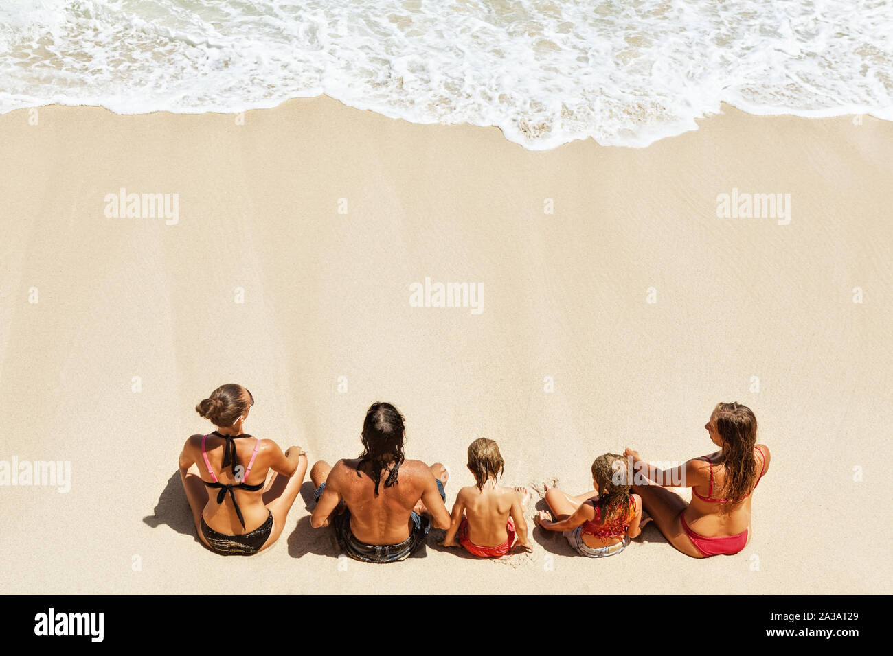 Sur sunny beach enfants heureux avec les parents s'amuser, s'asseoir sur le sable blanc voir en mer surf avec mousse et éclaboussures. Vue d'en haut. Les enfants de l'été, vie active Banque D'Images