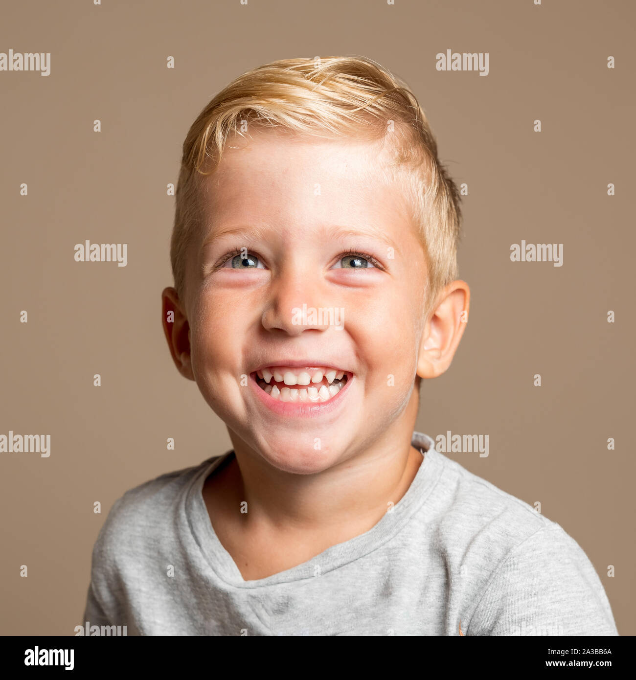 Close up of Baby Boy smiling trois ans, blonde aux yeux verts sur un fond brun clair, photo conceptuelle pour l'hygiène dentaire et les soins personnels. Banque D'Images