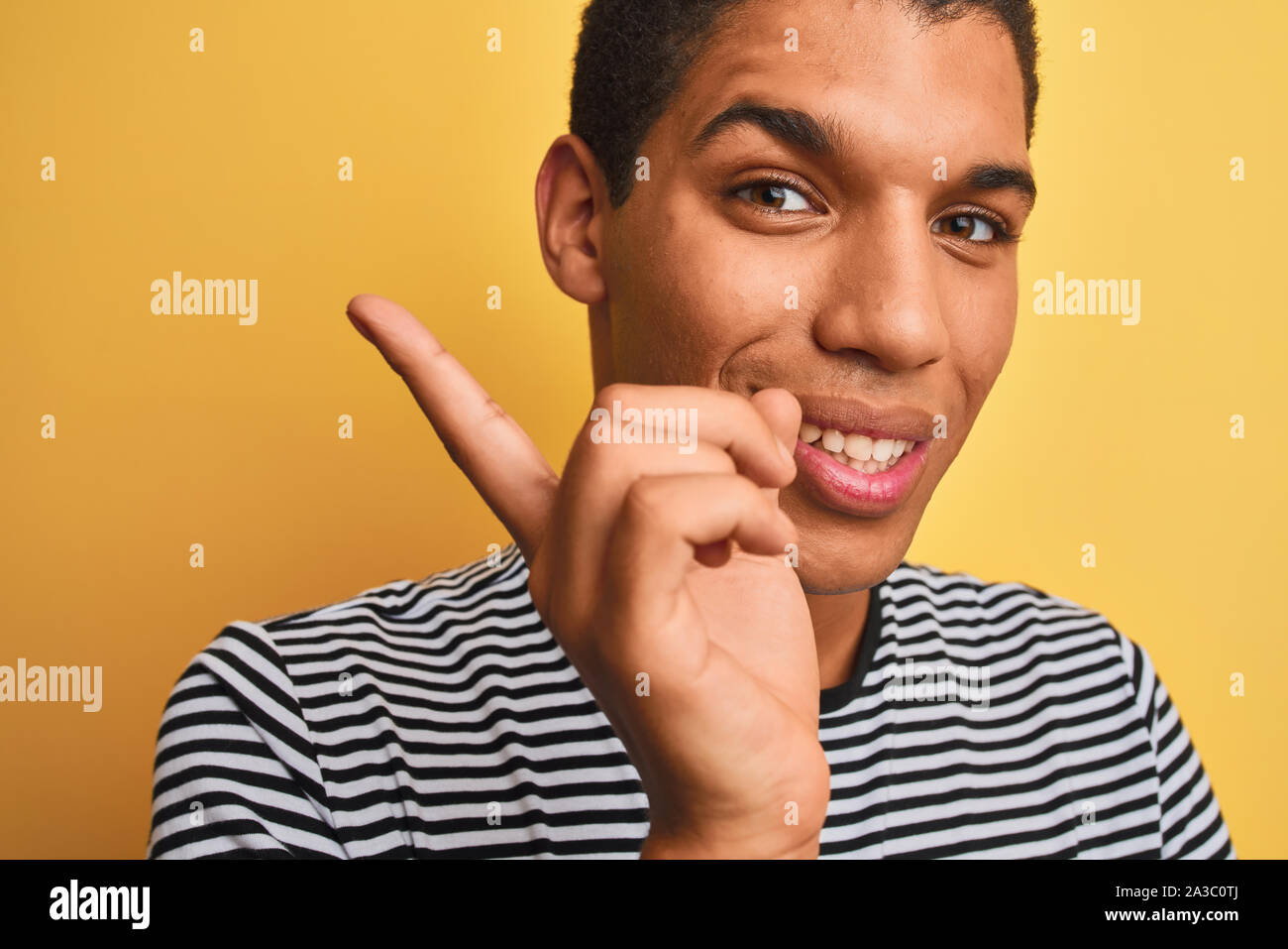 Beau jeune homme arabe portant des T-shirt à rayures marine isolé sur fond jaune très heureux pointant avec la main et le doigt sur le côté Banque D'Images