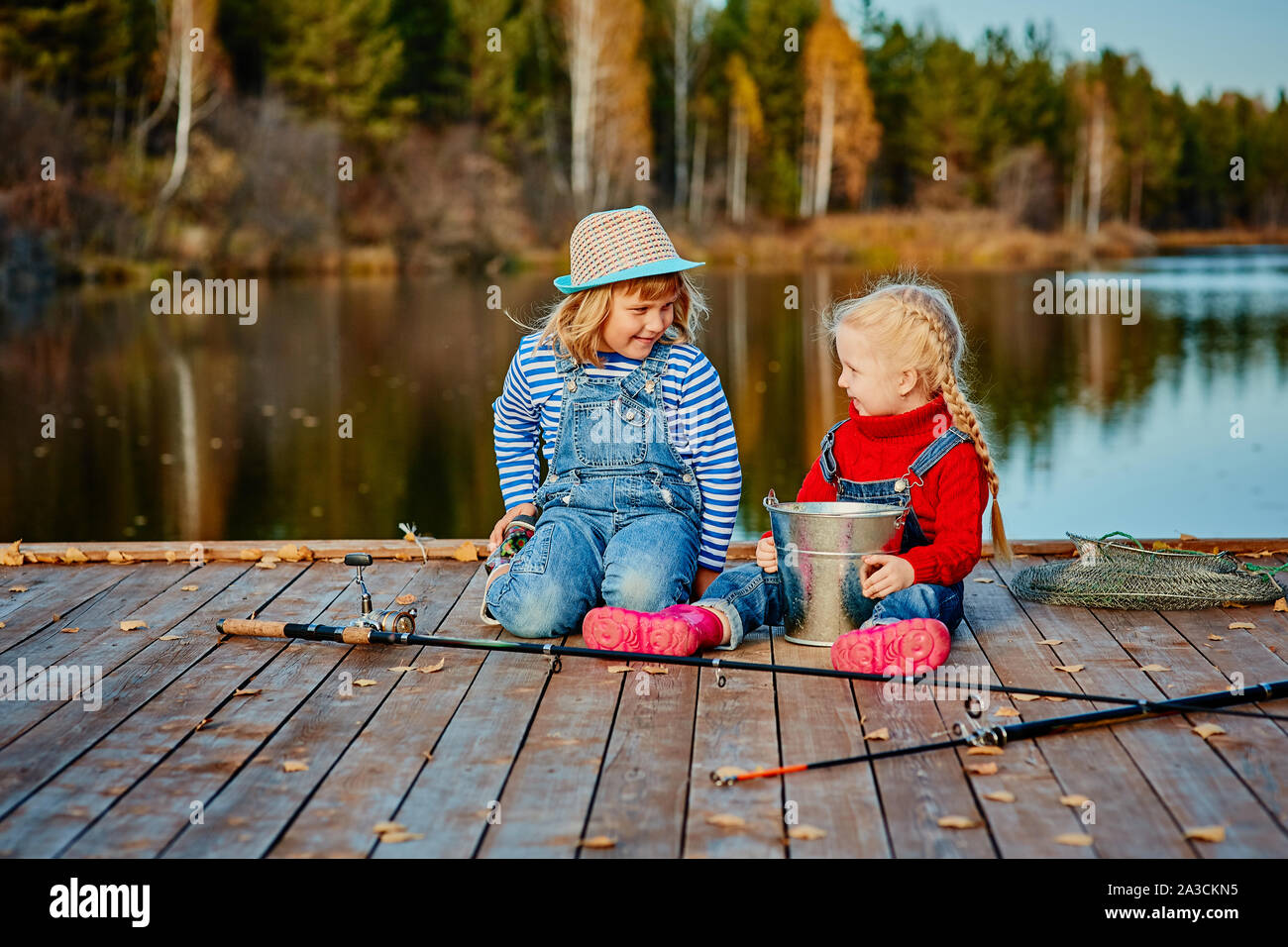 Deux petites sœurs ou vos amis de s'asseoir avec des cannes à pêche sur une jetée en bois. Ils ont attrapé un poisson et le mettre dans un seau. Ils sont heureux avec leurs prises et d Banque D'Images