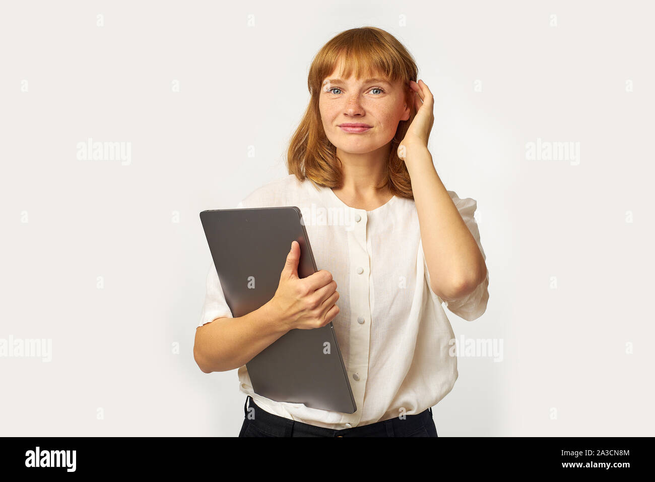 Portrait de jeune femme aux cheveux rouges et de rousseur holding laptop et à directement à l'appareil photo avec un sourire amical Banque D'Images