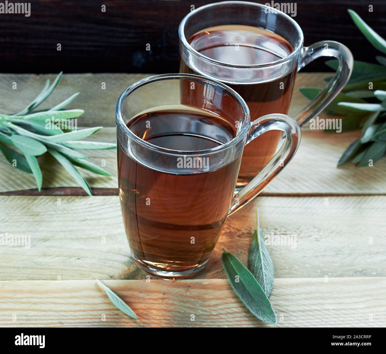 Tisane ou décoction de sauge dans une tasse en verre avec des feuilles d'herbes tout autour sur table en bois, gros plan, copiez l'espace, les boissons à base de plantes pour l'hiver concept Banque D'Images