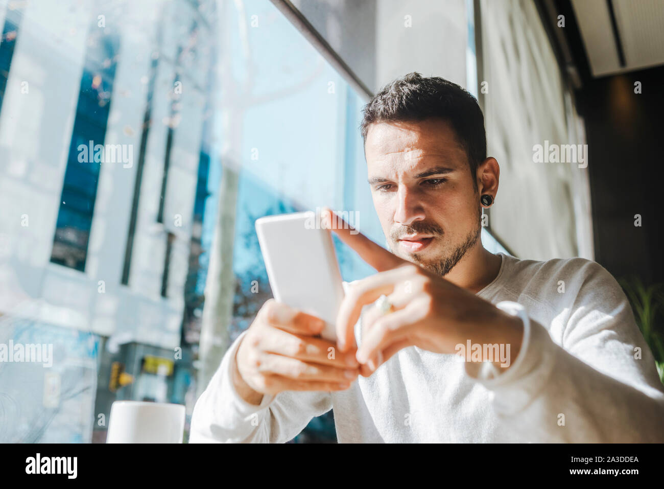 Smiling young man working in a cafe looking at cell phone Banque D'Images