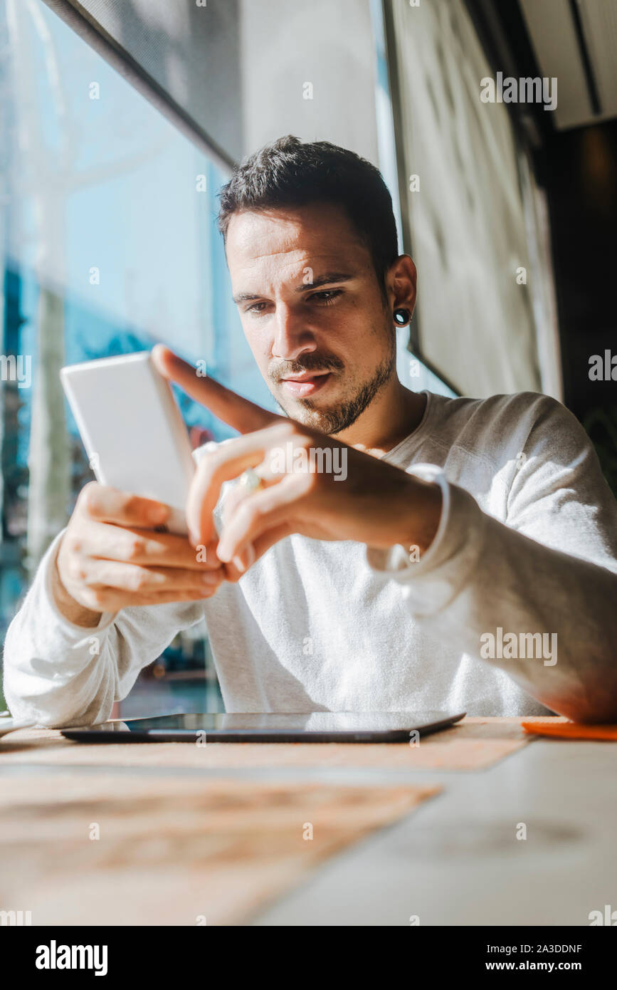 Smiling young man working in a cafe looking at cell phone Banque D'Images