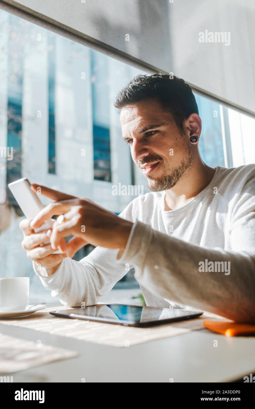 Smiling young man working in a cafe looking at cell phone Banque D'Images