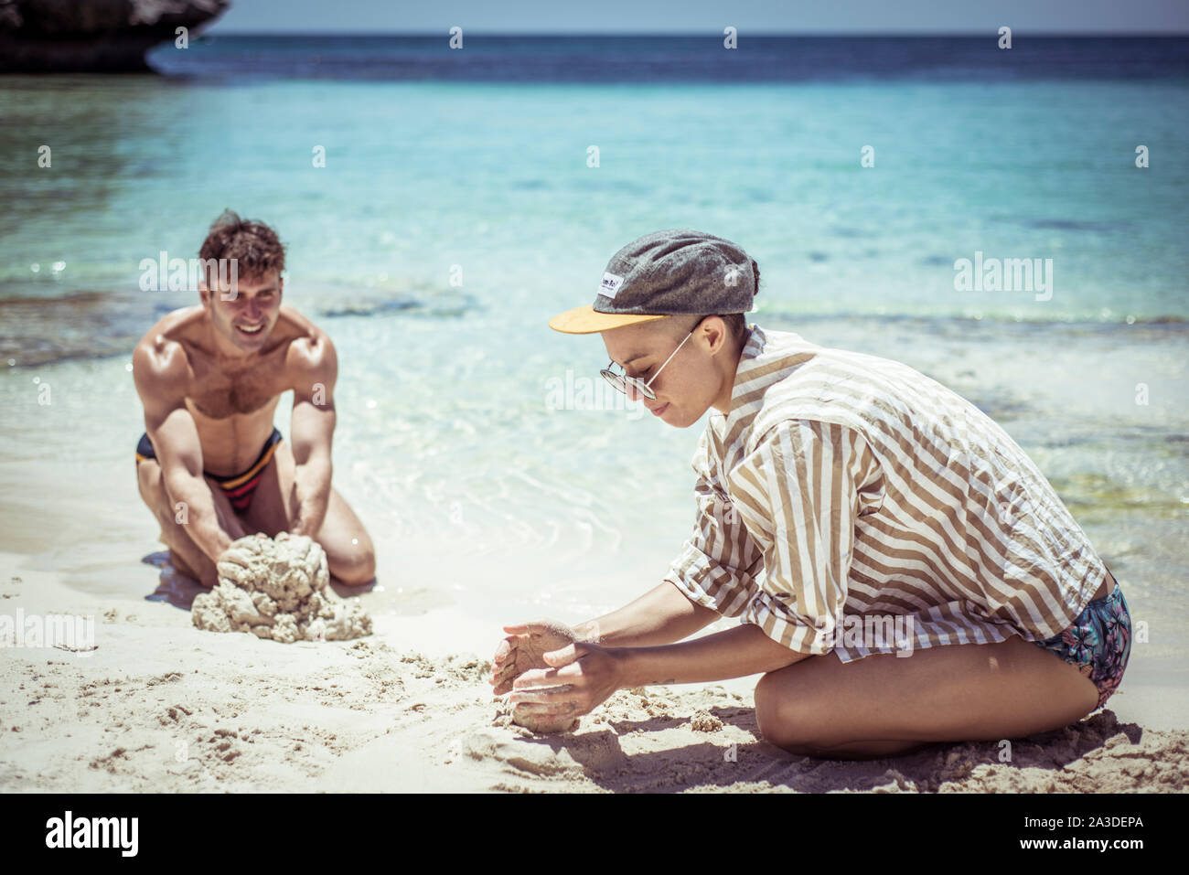 Jeune homme et femme, construire des châteaux de sable sur une plage bleue à Sun Banque D'Images