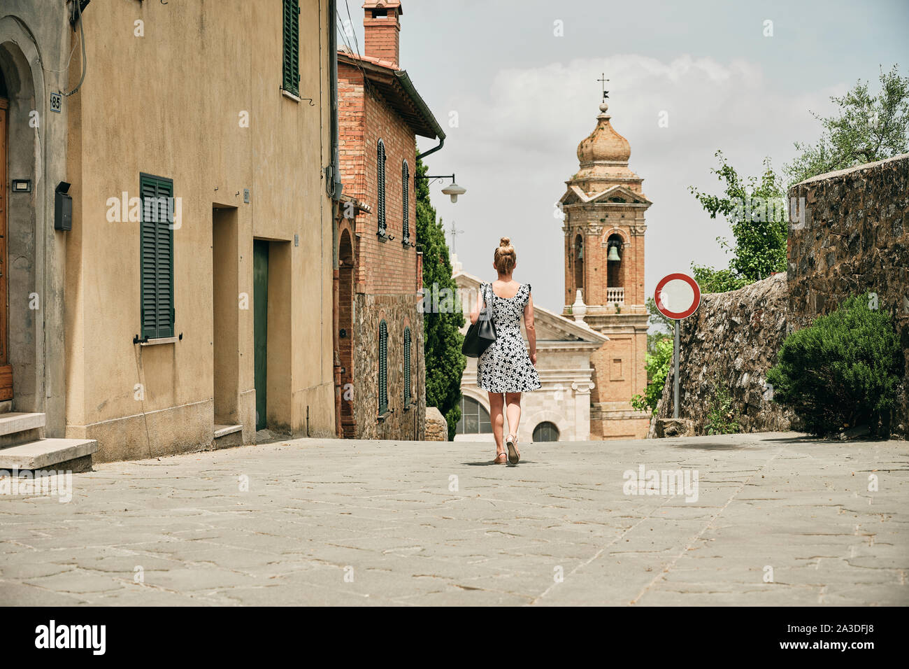 Vue arrière de la promenade femme marchant dans la rue pavée avec des maisons simples et l'interdiction de signer la circulation automobile avant de chapelle confortable en Toscane Italie Banque D'Images