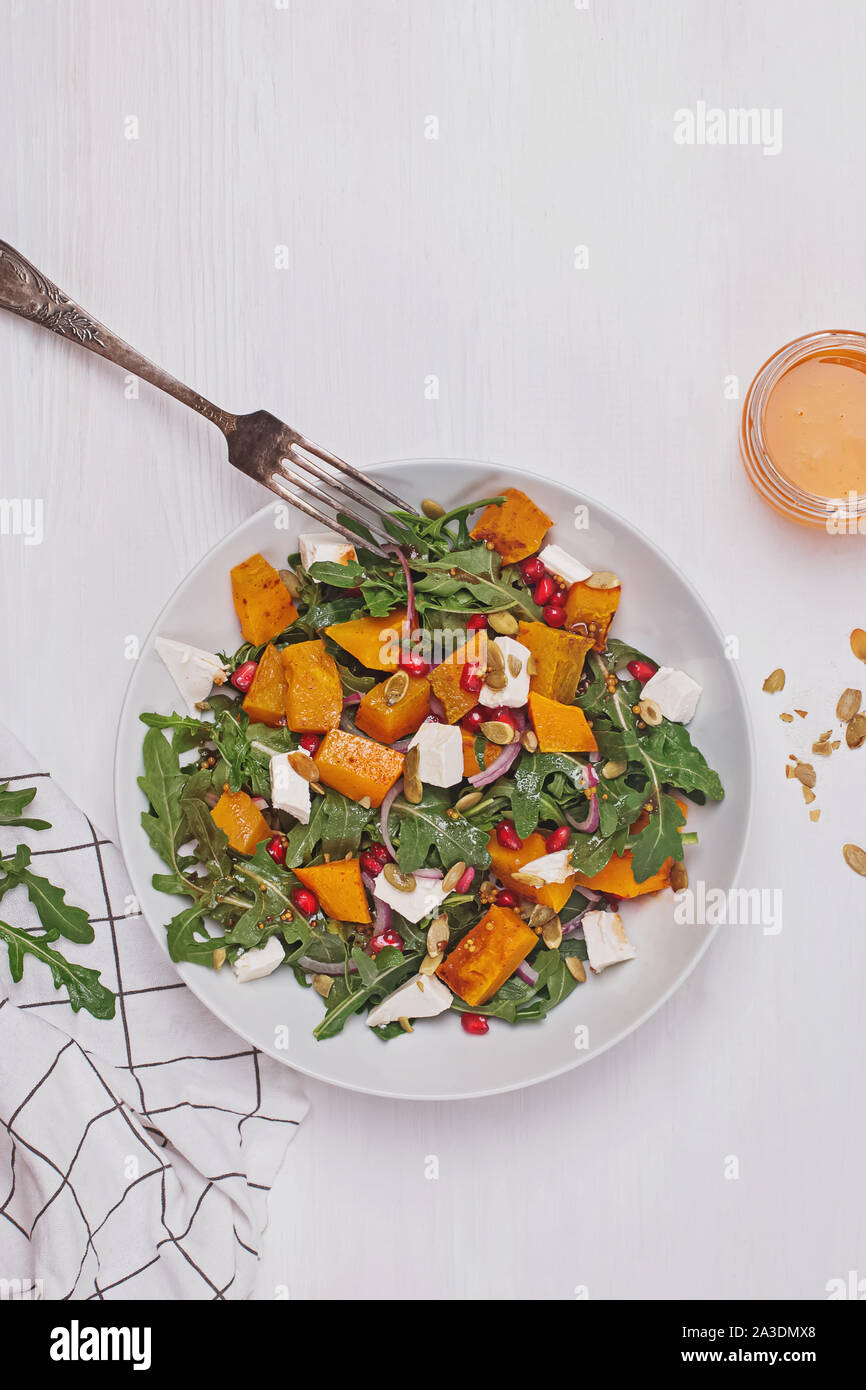 Avec salade de roquette, citrouille, fromage feta et graines de grenade sur table en bois blanc Banque D'Images