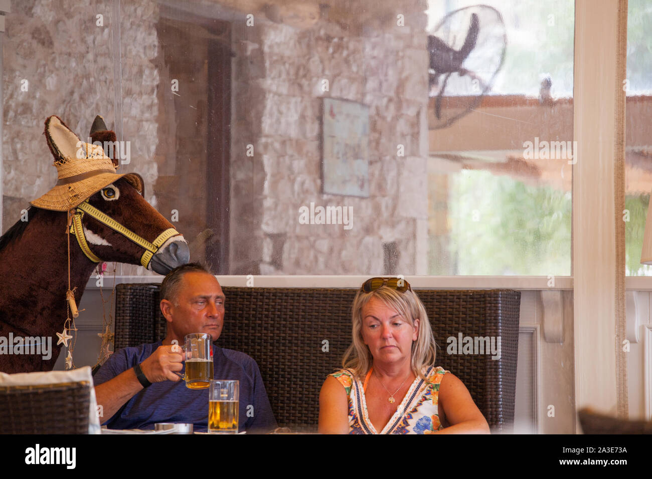 L'homme et la femme assis à boire à taverne grecque à côté d'un âne en peluche modèle dans un chapeau de paille Banque D'Images