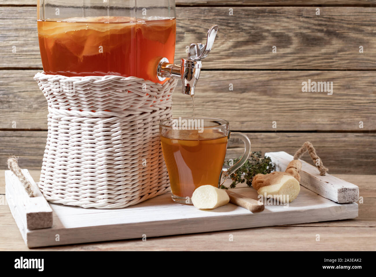 Des kombucha fermenté verre dans un pot avec robinet et dans une tasse sur un plateau blanc sur un fond de bois, copyspace. Banque D'Images