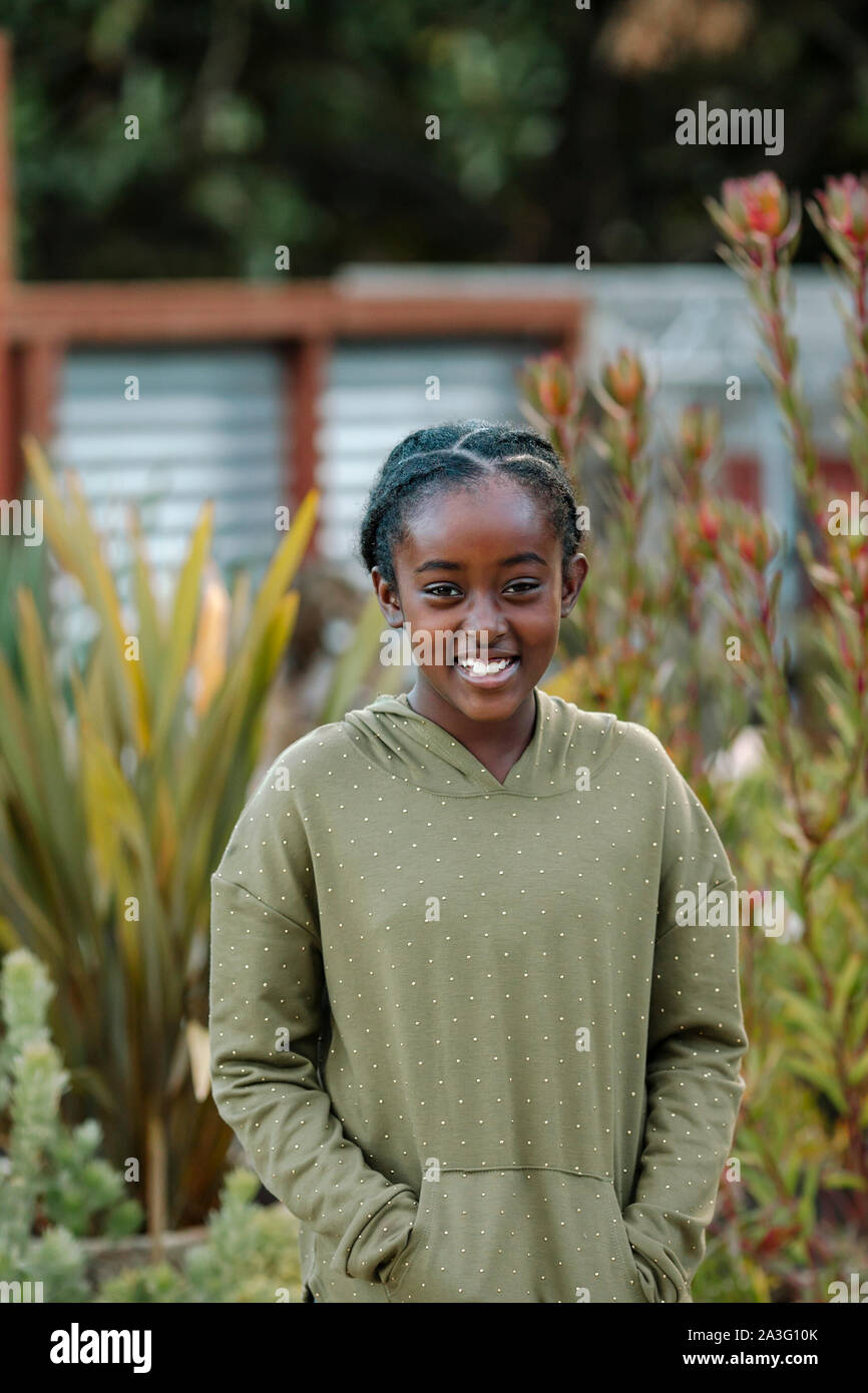 Pretty smiling black girl in une capuche à pois par de grandes plantes Banque D'Images