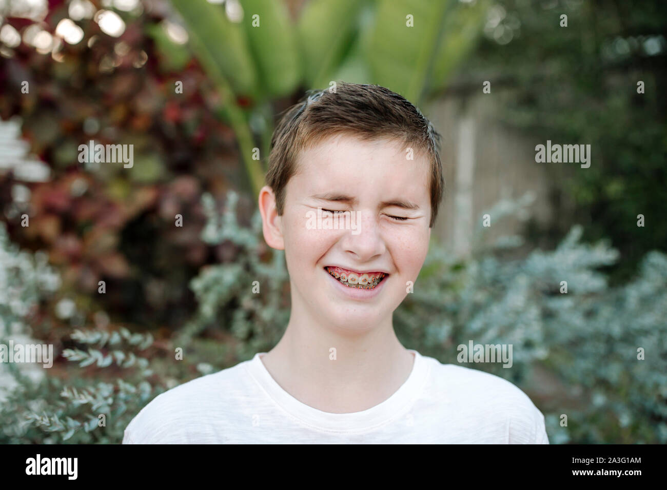 Rire preteen boy avec les cheveux courts et les accolades près de plantes luxuriantes Banque D'Images