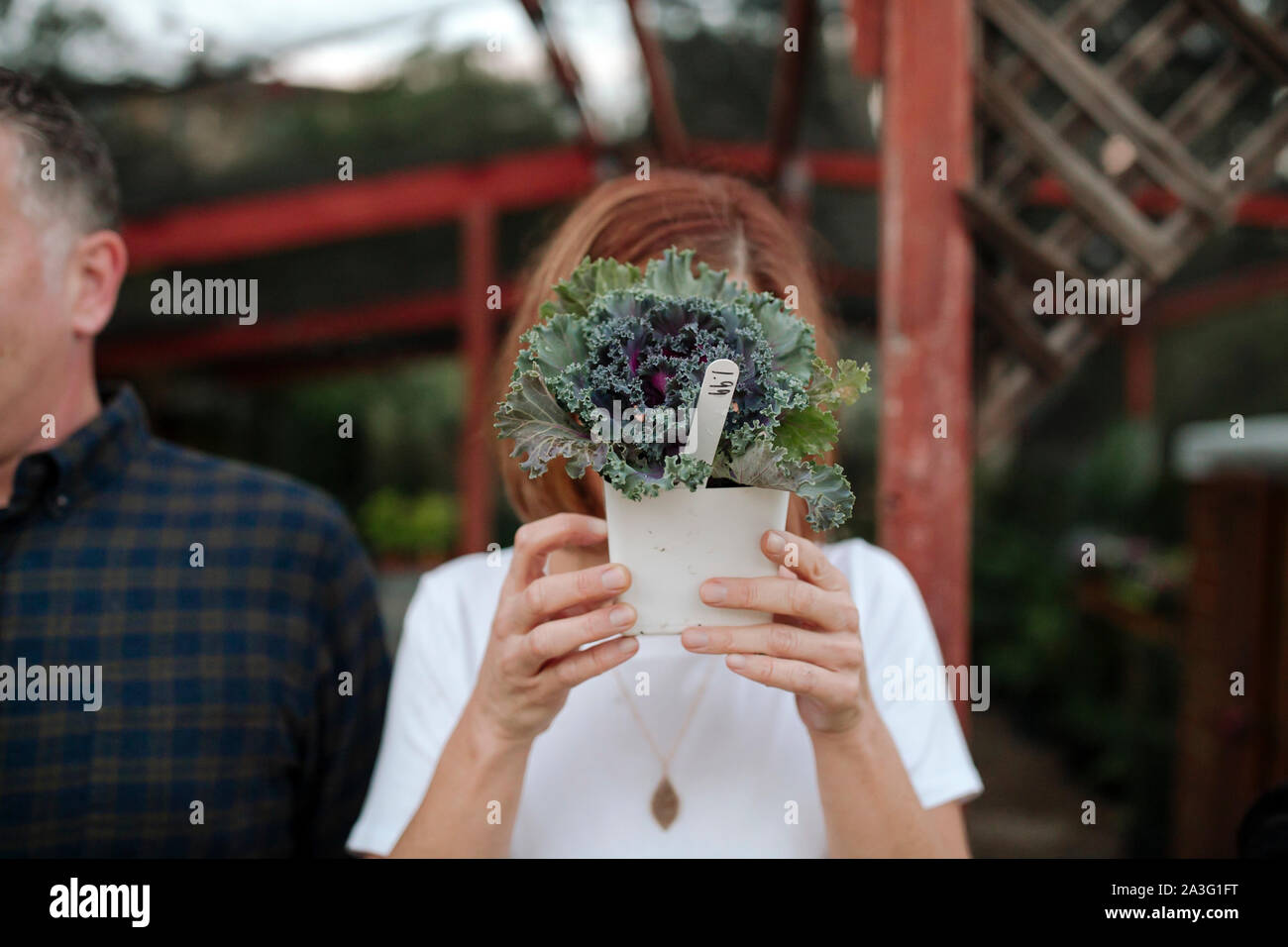Red-haired woman wearing white shirt holding plant in front of face Banque D'Images