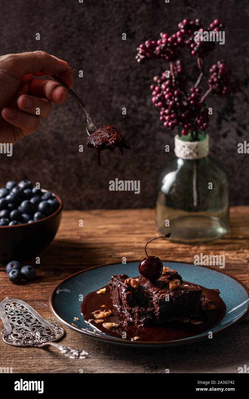 Homme de race blanche part en prenant un morceau d'un brownie au chocolat végétalien avec une fourche de pâtisserie, sauce chocolat est dégoulinant sur un brownie humide Banque D'Images