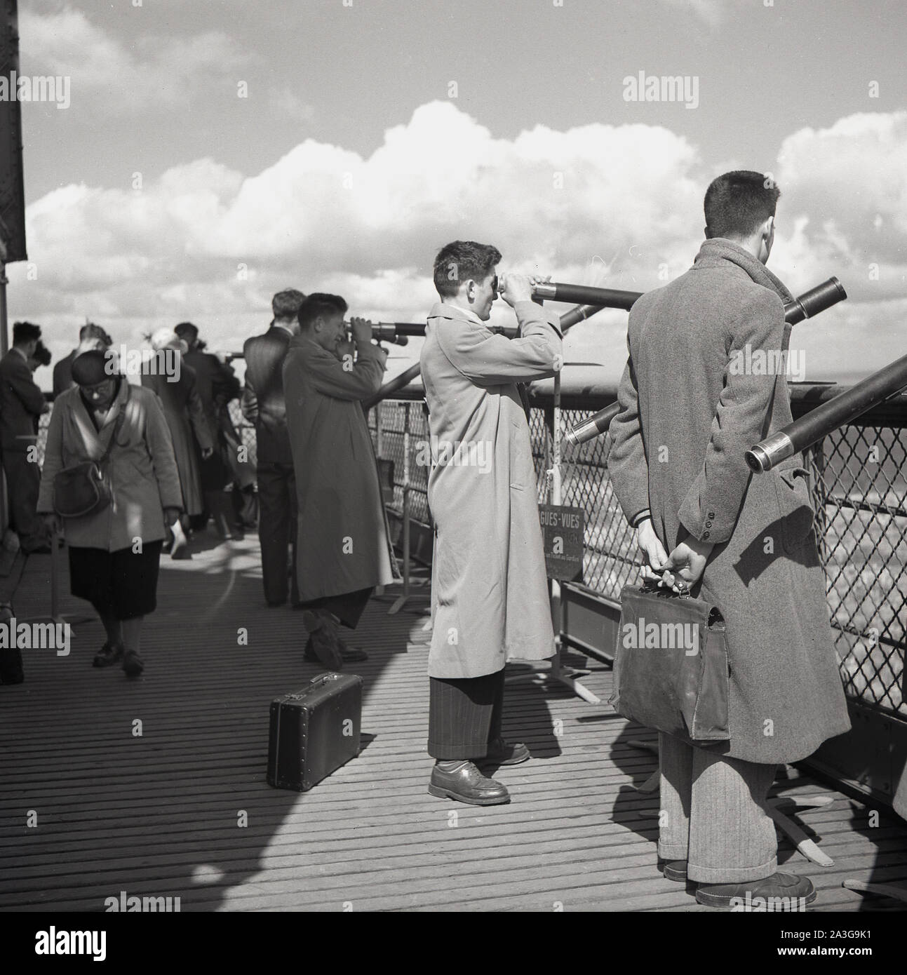 Années 1950, historiques, les gens sur la plate-forme en bois en haut de la Tour Eiffel en utilisant les 20 'franc' Longues-Vues ou télescopes pour regarder au-dessus de la ville de Paris, France. Banque D'Images