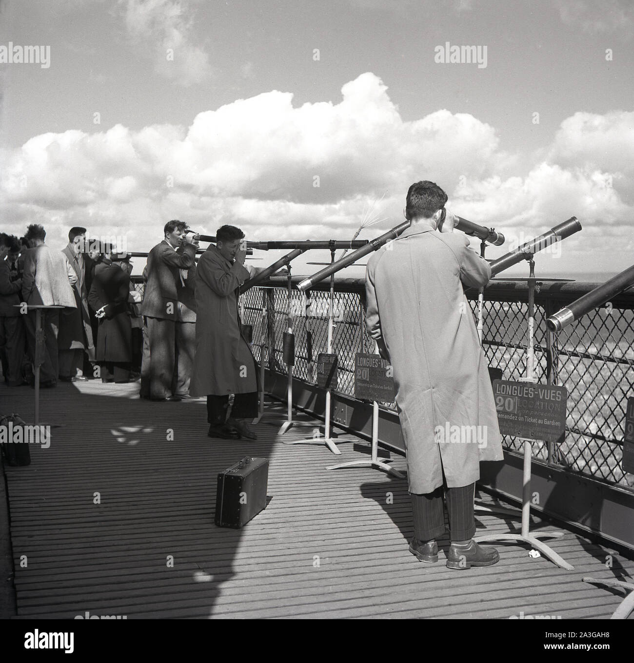 Années 1950, historiques, les gens sur la plate-forme en bois en haut de la Tour Eiffel en utilisant les 20 'franc' Longues-Vues ou télescopes pour regarder au-dessus de la ville de Paris, France. Banque D'Images