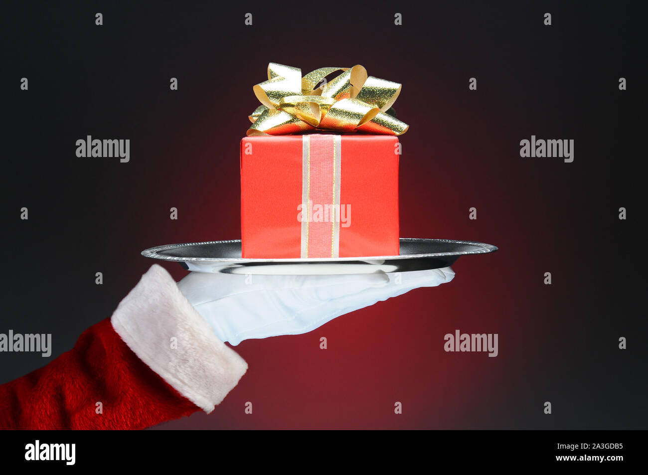 Père Noël tenant un plateau avec un wrapped present. Mains et bras seulement sur un fond rouge clair à foncé. Banque D'Images Père Noël tenant un plateau avec un wrapped present. Mains et bras seulement sur un fond rouge clair à foncé. Banque D'Images