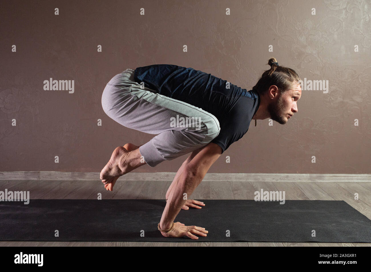 Jeune homme sportif pratiquant le yoga, la méditation en demi-lotus pose, travailler, le port des vêtements de sport, piscine pleine longueur, brown yoga studio Banque D'Images