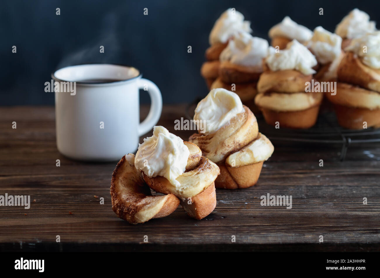 Des frais de hauteur à la cannelle avec glaçage fromage à la crème. La vapeur chaude tasse de café dans l'arrière-plan avec plus de pains sur un rack boulangers. Banque D'Images