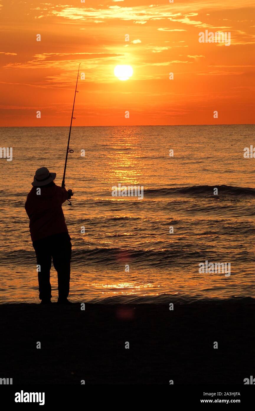 Pêcheur silhouette sur la plage au coucher du soleil Banque D'Images