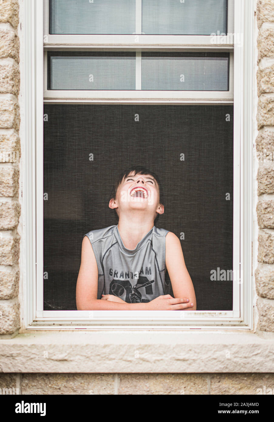Jeune garçon riant dans une fenêtre ouverte d'une balle dans l'écran. Banque D'Images