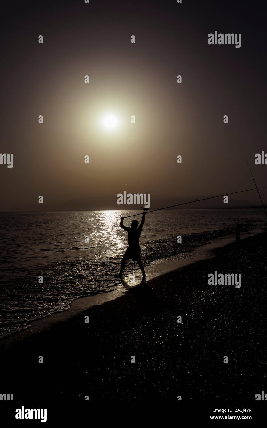 Silhouette de pêcheur sur la plage avec tige de poisson l'article sur l'eau de mer au coucher du soleil de pêche avec de belles vacances dans le ciel d'or et passe-temps détente lei Banque D'Images