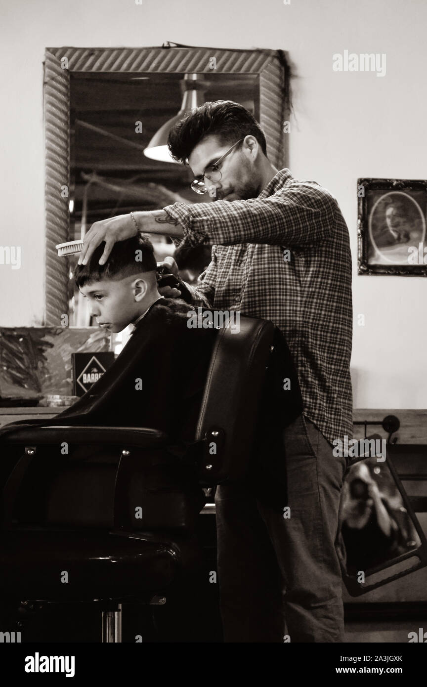 Avec un garçon est assis dans l'aire de coiffeur tout en ayant tendance à coupe de la hanche '81 barbiers shop à Tucson, AZ, en sépia Banque D'Images